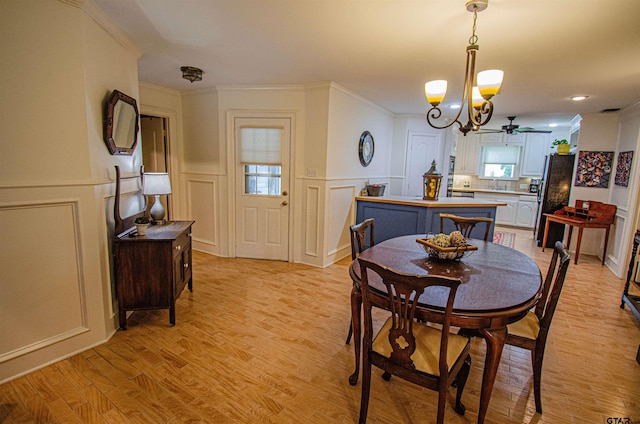 dining space with light hardwood / wood-style floors, ceiling fan with notable chandelier, sink, and crown molding