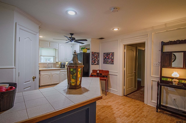 kitchen with tile countertops, white cabinetry, ceiling fan, light hardwood / wood-style flooring, and black refrigerator