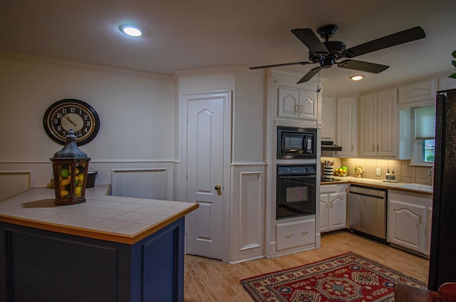 kitchen featuring black appliances, ornamental molding, light hardwood / wood-style floors, tile countertops, and ceiling fan