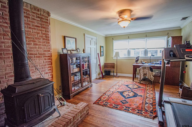 office area with a wood stove, wood-type flooring, ceiling fan, and crown molding