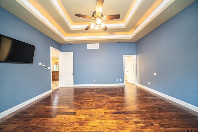 empty room featuring ornamental molding, a raised ceiling, ceiling fan, and dark wood-type flooring