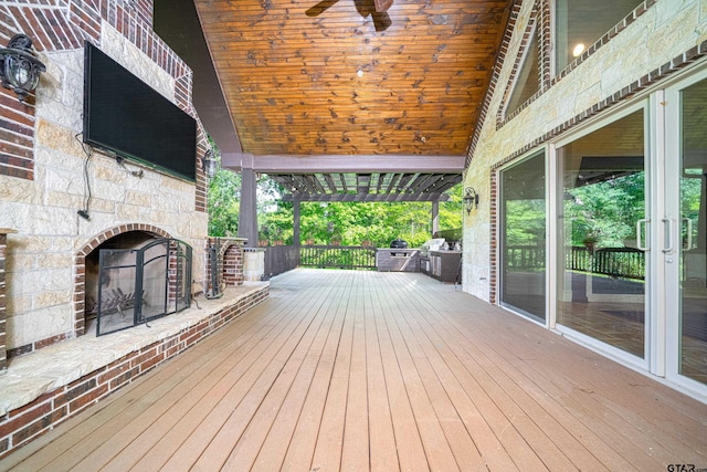 wooden terrace with a large fireplace, ceiling fan, and a pergola