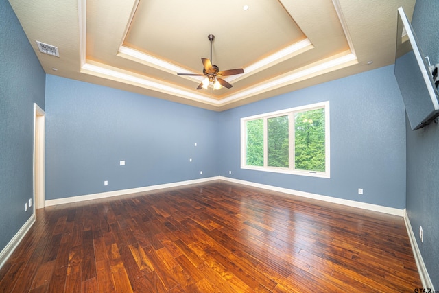 empty room featuring a tray ceiling, ceiling fan, and dark hardwood / wood-style floors