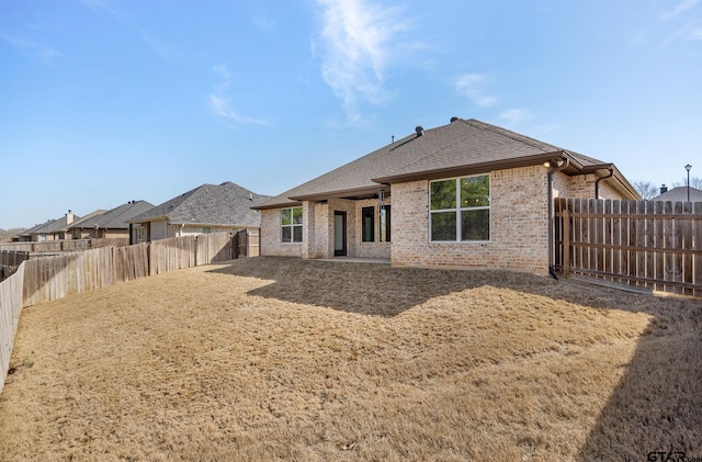 rear view of property featuring brick siding, a fenced backyard, and roof with shingles