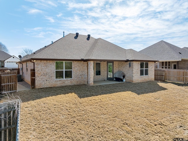 rear view of property with brick siding, roof with shingles, a fenced backyard, and a patio area