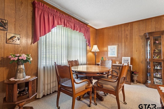 dining area with wood walls, a textured ceiling, light colored carpet, and crown molding