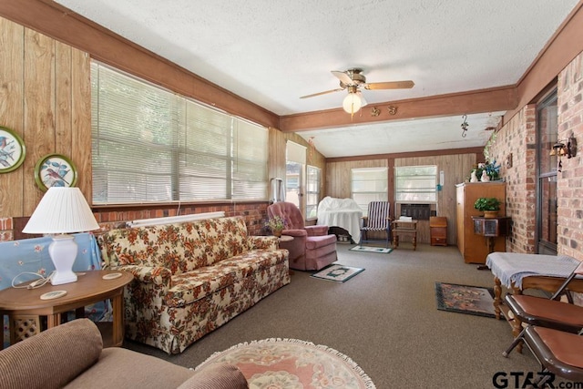 carpeted living room featuring a textured ceiling, wooden walls, vaulted ceiling with beams, and ceiling fan