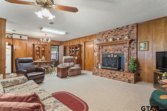 carpeted living room with wood walls, ceiling fan, a textured ceiling, and a wood stove