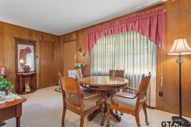 dining room with wood walls, a textured ceiling, light carpet, and ornamental molding