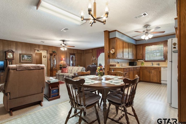 dining space with ceiling fan with notable chandelier, wood walls, a textured ceiling, and sink