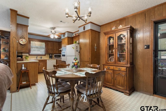 dining space featuring wood walls, a textured ceiling, and ceiling fan with notable chandelier