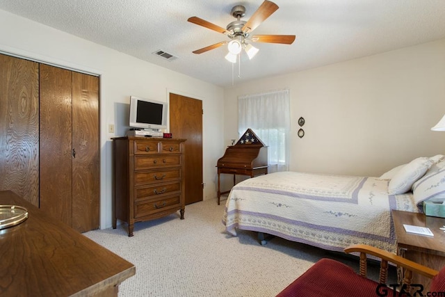 bedroom with a textured ceiling, light carpet, ceiling fan, and a closet