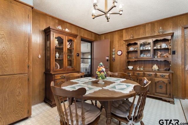 dining room with wood walls, a textured ceiling, an inviting chandelier, and ornamental molding