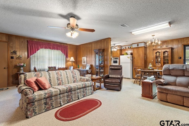 carpeted living room with wood walls, ceiling fan with notable chandelier, and a textured ceiling