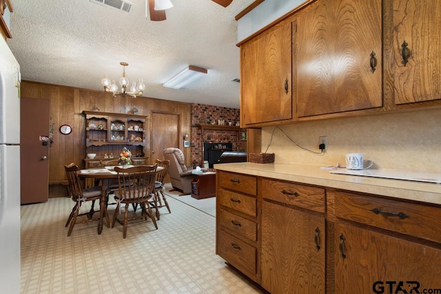 kitchen featuring wood walls, ceiling fan with notable chandelier, a textured ceiling, decorative light fixtures, and a fireplace