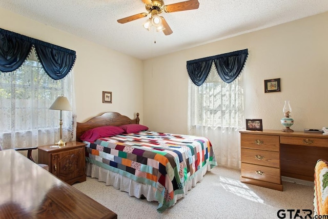 bedroom featuring a textured ceiling, light colored carpet, multiple windows, and ceiling fan