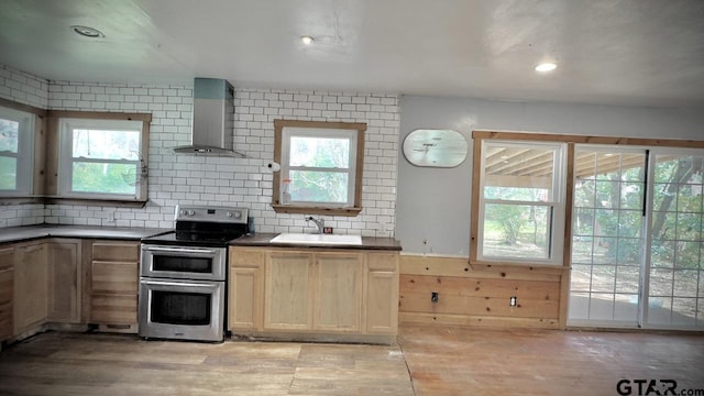 kitchen with a wealth of natural light, stainless steel range with electric cooktop, wall chimney exhaust hood, and sink