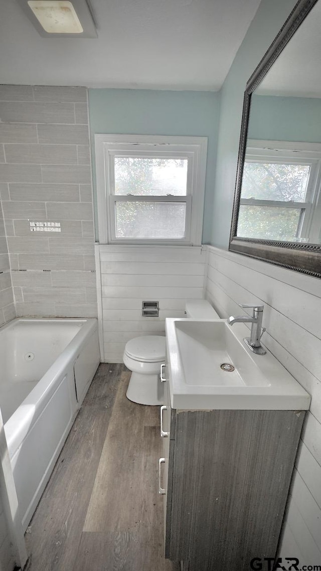 bathroom featuring wood walls, wood-type flooring, toilet, a bathtub, and vanity