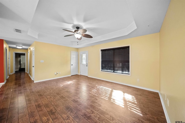 empty room with dark wood-type flooring, a raised ceiling, and ceiling fan