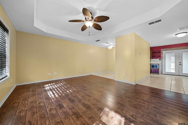 unfurnished living room featuring french doors, ceiling fan, wood-type flooring, and a tray ceiling