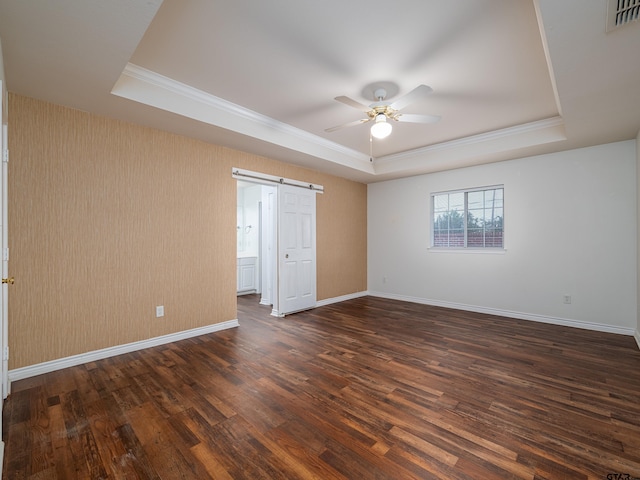 unfurnished bedroom featuring dark wood-type flooring, a barn door, ceiling fan, and a tray ceiling