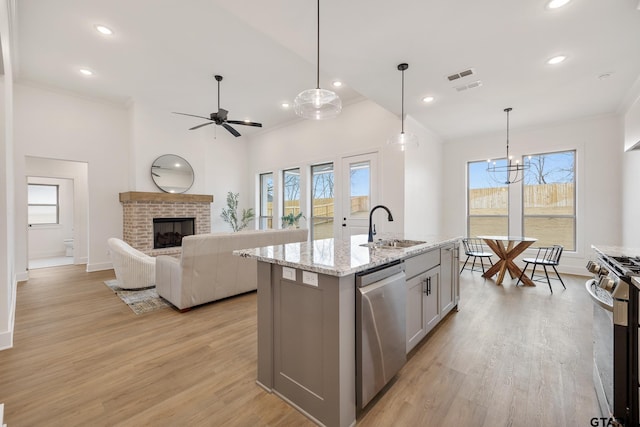 kitchen with appliances with stainless steel finishes, sink, hanging light fixtures, a kitchen island with sink, and light stone counters