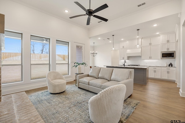 living room with ceiling fan with notable chandelier, sink, crown molding, and light wood-type flooring