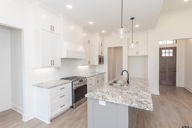 kitchen featuring appliances with stainless steel finishes, white cabinetry, a kitchen island with sink, sink, and decorative light fixtures