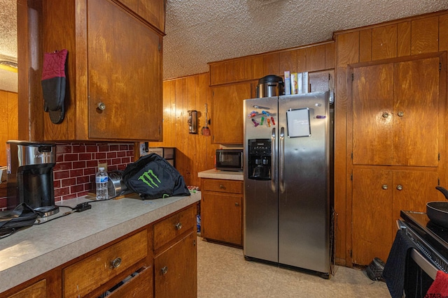 2114 Martin Luther King Blvd, Palestine, TX 75803 - kitchen with stainless steel fridge with ice dispenser, brown cabinets, black microwave, wooden walls, and a textured ceiling