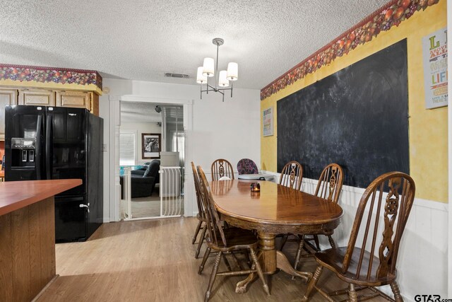 dining area featuring a wainscoted wall, visible vents, light wood-style floors, a textured ceiling, and a chandelier