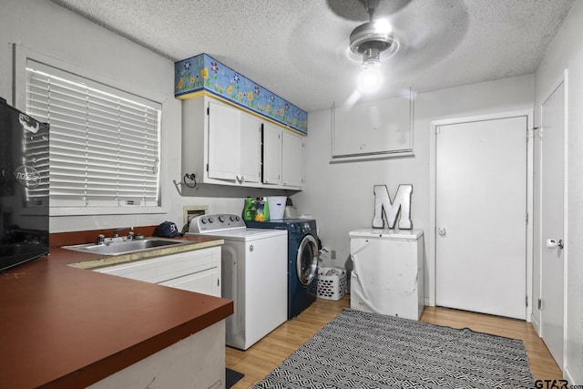 laundry room featuring cabinet space, washer and clothes dryer, a textured ceiling, light wood-style floors, and a sink