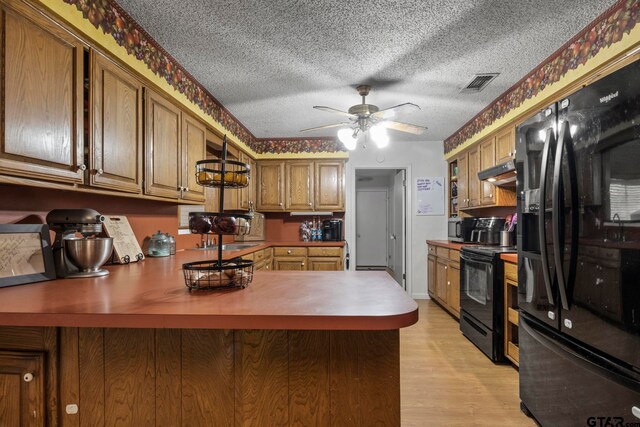 kitchen featuring visible vents, under cabinet range hood, black appliances, and a peninsula