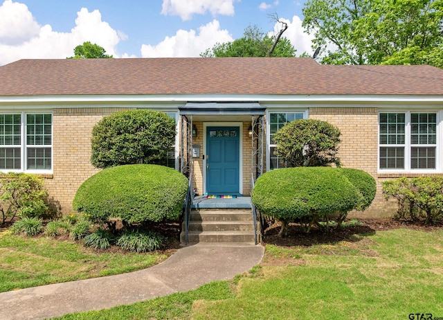 view of front facade with roof with shingles, a front lawn, and brick siding