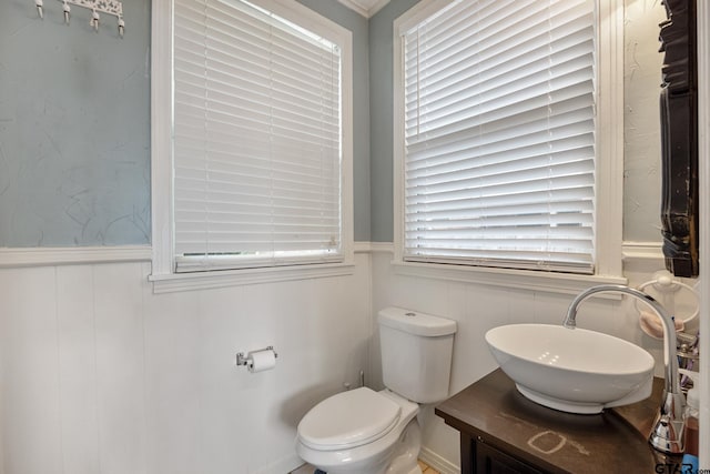 half bathroom with vanity, wainscoting, toilet, and a decorative wall