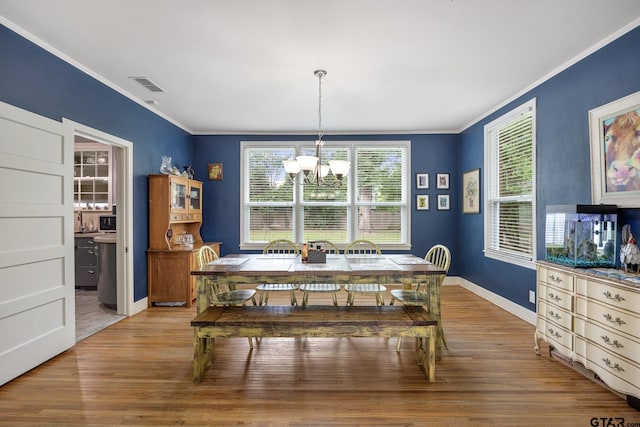 dining space featuring an inviting chandelier, ornamental molding, wood finished floors, and visible vents