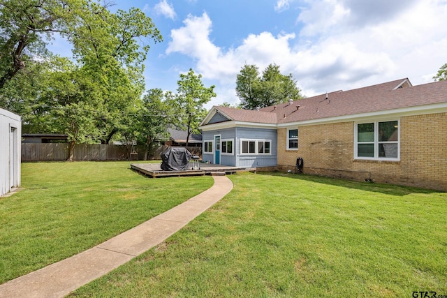 back of property featuring a wooden deck, brick siding, fence, a yard, and a shingled roof