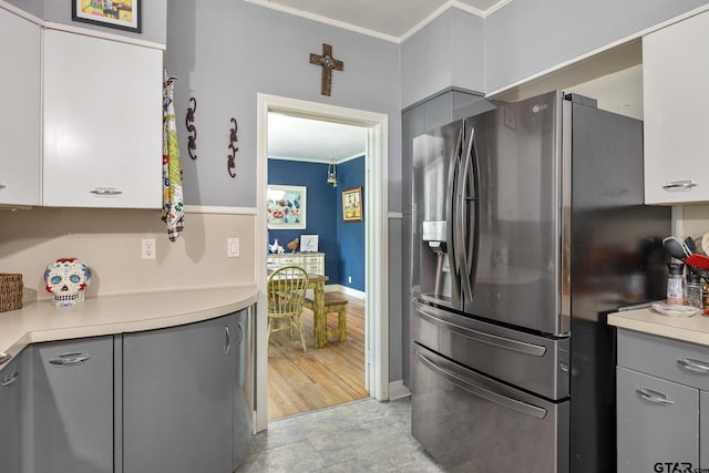 kitchen featuring crown molding, stainless steel refrigerator with ice dispenser, baseboards, and light countertops