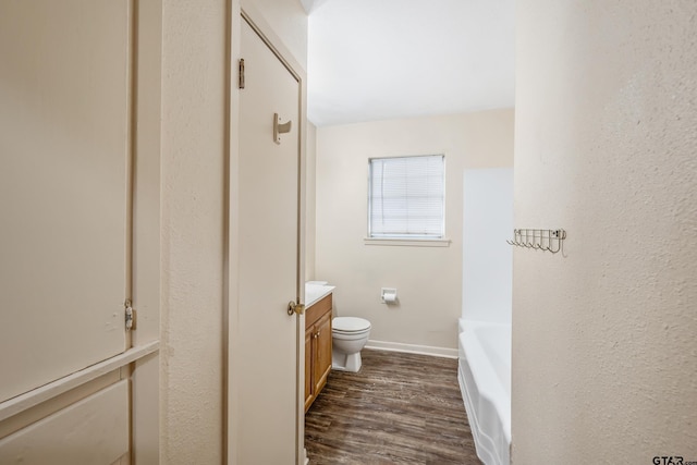 bathroom with vanity, wood finished floors, a bathtub, toilet, and baseboards