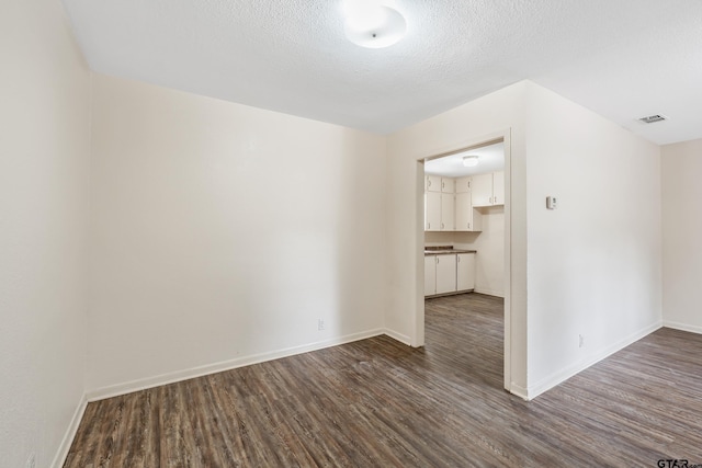 spare room featuring dark wood-style flooring, baseboards, and a textured ceiling
