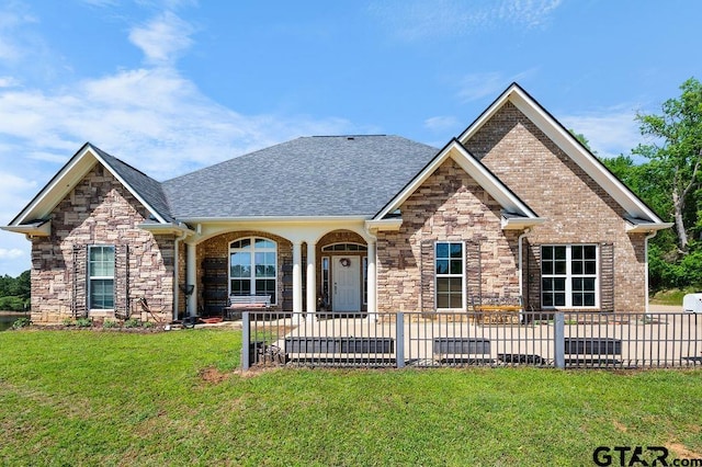 craftsman-style home featuring fence, a front lawn, roof with shingles, and stone siding