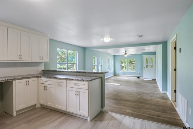 kitchen featuring white cabinetry, light stone countertops, light wood-type flooring, and kitchen peninsula