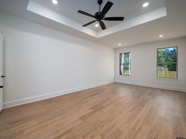 unfurnished room featuring a raised ceiling, ceiling fan, and light hardwood / wood-style flooring