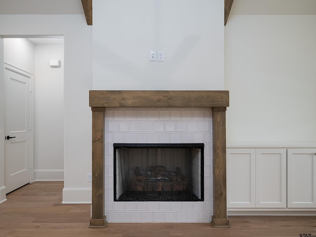 interior details featuring beam ceiling, wood-type flooring, and a tiled fireplace