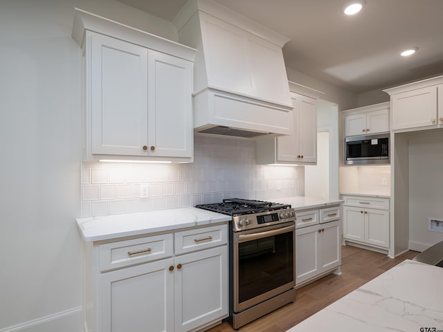 kitchen featuring light hardwood / wood-style flooring, light stone countertops, tasteful backsplash, custom range hood, and stainless steel appliances