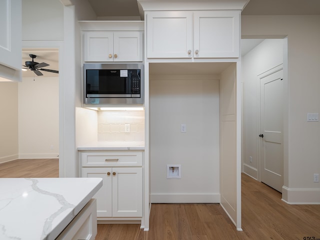 kitchen with stainless steel microwave, tasteful backsplash, light stone counters, light hardwood / wood-style flooring, and white cabinets