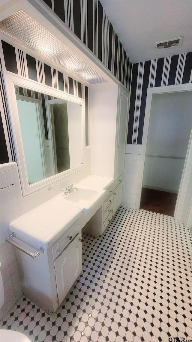 bathroom featuring wallpapered walls, a wainscoted wall, tile walls, and vanity