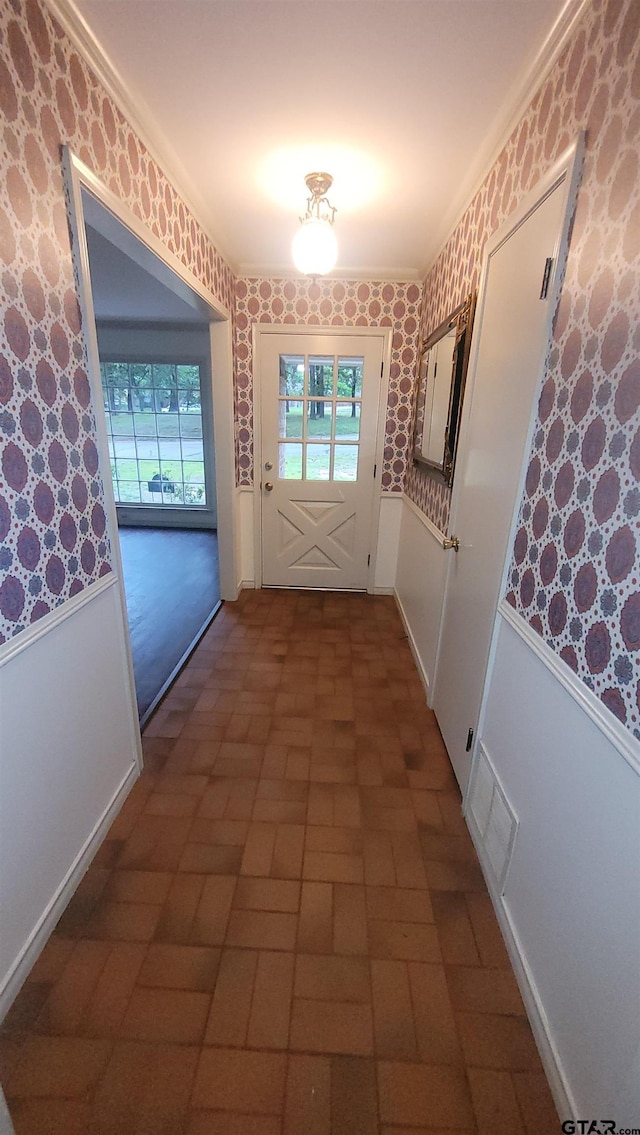 entryway featuring brick patterned flooring, wallpapered walls, a wainscoted wall, plenty of natural light, and ornamental molding