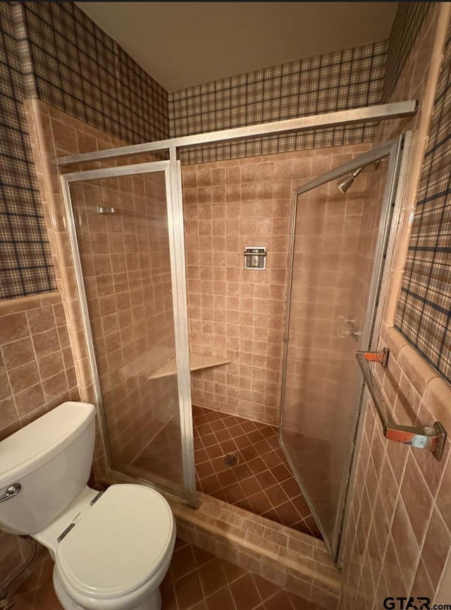 full bath with tile walls, a shower stall, toilet, and tile patterned flooring