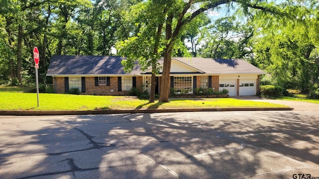 ranch-style home featuring driveway, a front yard, a garage, and brick siding