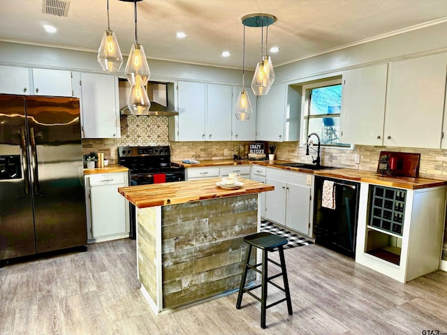 kitchen with pendant lighting, wall chimney range hood, white cabinets, and black appliances